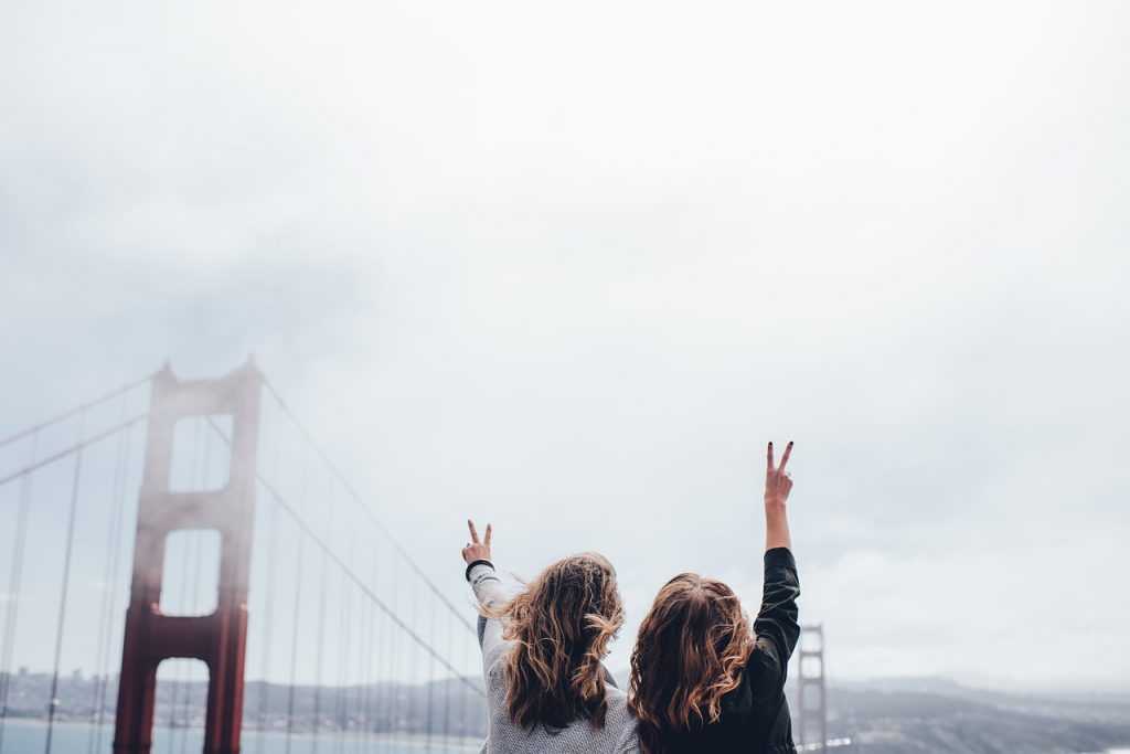 two women giving the peace sign facing the Golden Gate bridge in San Francisco