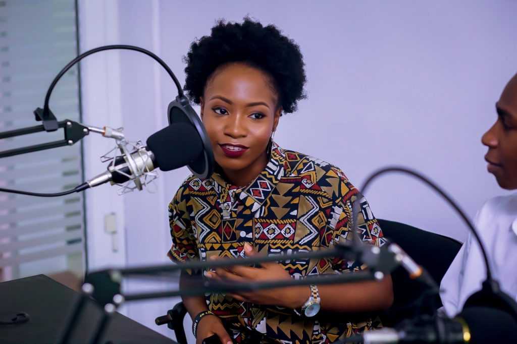 nicely dressed woman at a desk leaning toward podcast microphone